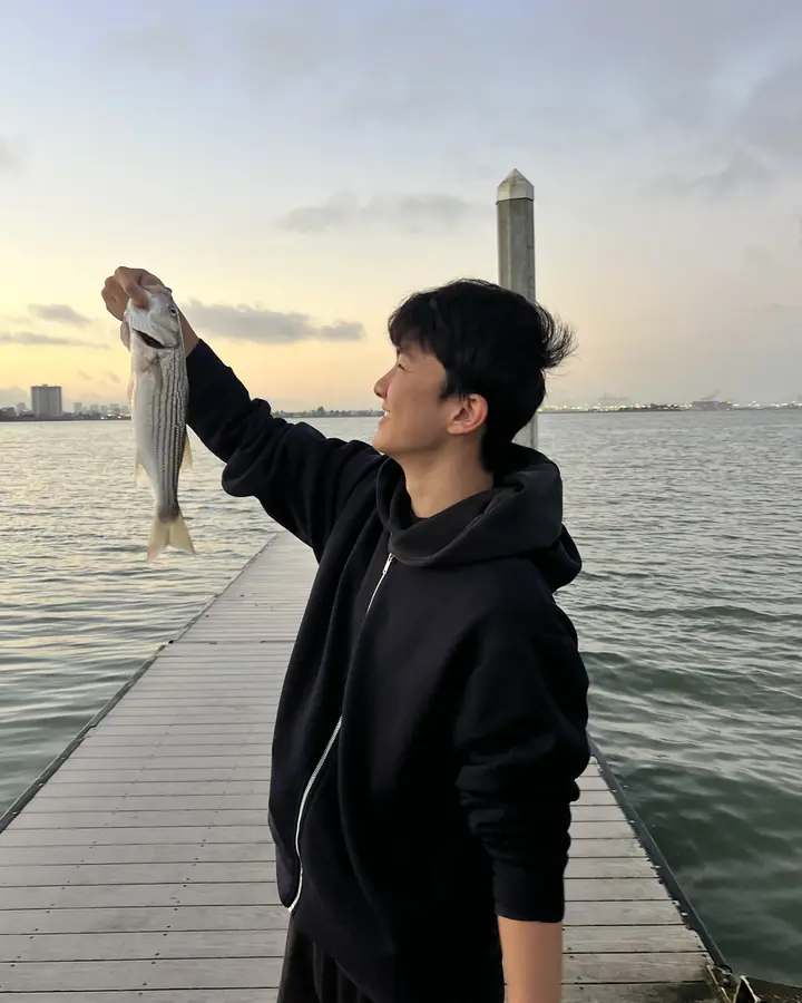 Justin on a pier at sunset, holding up a fish